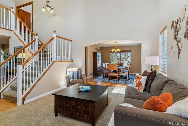 carpeted living room with an inviting chandelier, baseboards, stairway, and arched walkways