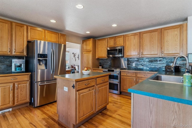 kitchen featuring stainless steel appliances, a kitchen island, a sink, light wood-style floors, and dark countertops