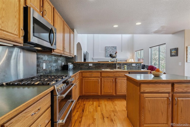 kitchen with stainless steel appliances, decorative backsplash, light wood-style floors, a sink, and a peninsula