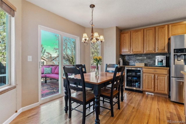 dining room with an inviting chandelier, beverage cooler, baseboards, and light wood-style flooring