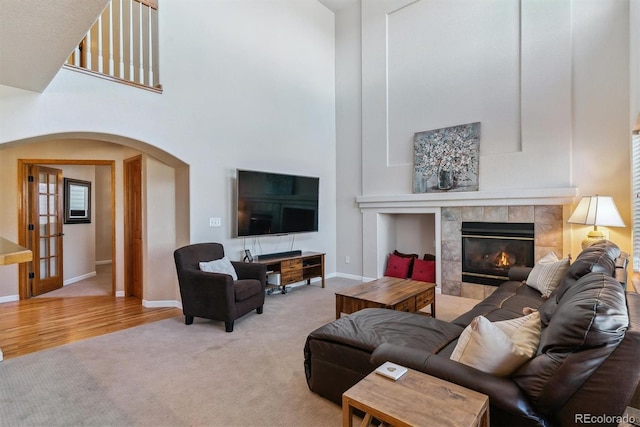 carpeted living area with baseboards, a high ceiling, arched walkways, and a tiled fireplace