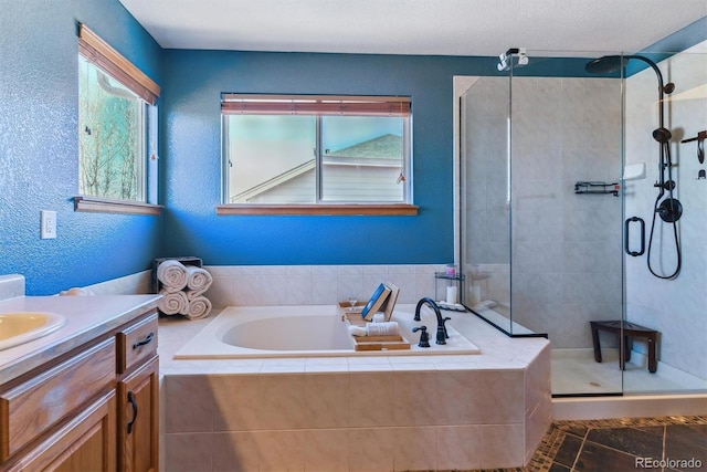 full bathroom with a stall shower, vanity, a bath, and a textured wall