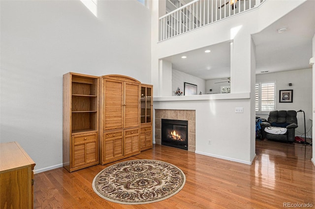 living room with ceiling fan, a fireplace, a towering ceiling, and wood-type flooring