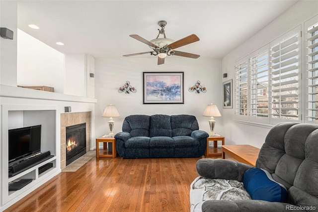 living room featuring a tile fireplace, wood-type flooring, and ceiling fan