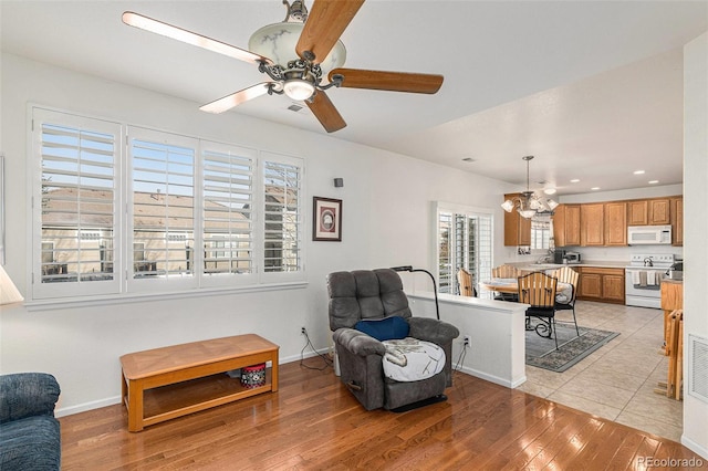 living room featuring plenty of natural light, ceiling fan with notable chandelier, and light hardwood / wood-style flooring