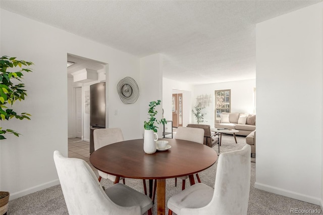 dining room with a textured ceiling, light colored carpet, and baseboards