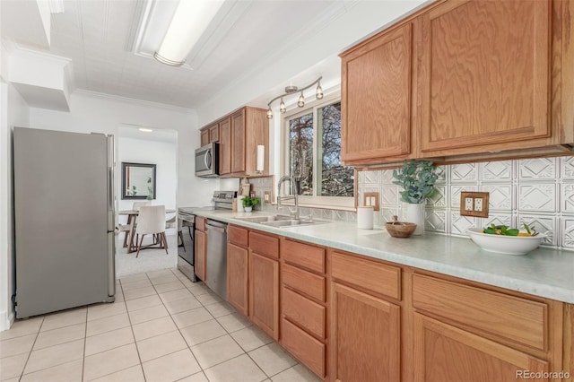 kitchen with light tile patterned floors, a sink, light countertops, appliances with stainless steel finishes, and crown molding