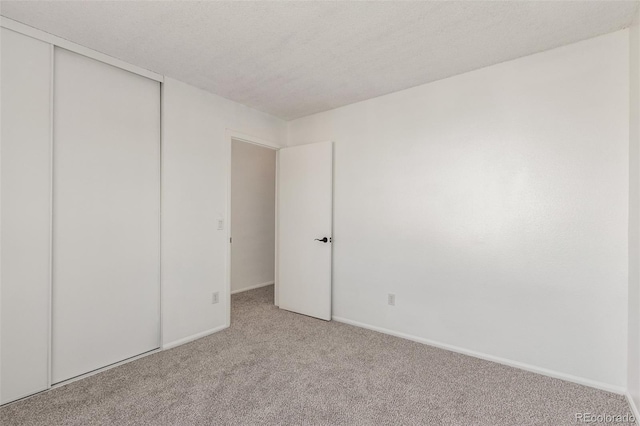 unfurnished bedroom featuring light carpet, a closet, baseboards, and a textured ceiling