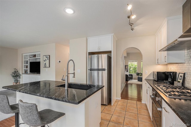 3289 Cummings Dr, Erie, CO 80516 - kitchen featuring appliances with stainless steel finishes, wall chimney range hood, arched walkways, white cabinets, and decorative backsplash