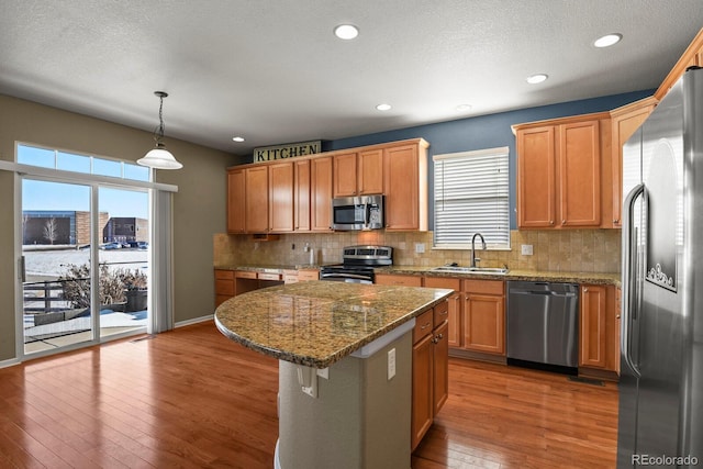 kitchen featuring sink, appliances with stainless steel finishes, decorative light fixtures, a kitchen island, and light stone counters