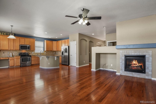 kitchen featuring pendant lighting, decorative backsplash, appliances with stainless steel finishes, a kitchen bar, and a tiled fireplace