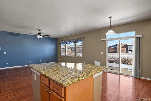 kitchen featuring light stone countertops, a center island, ceiling fan, dark hardwood / wood-style floors, and pendant lighting