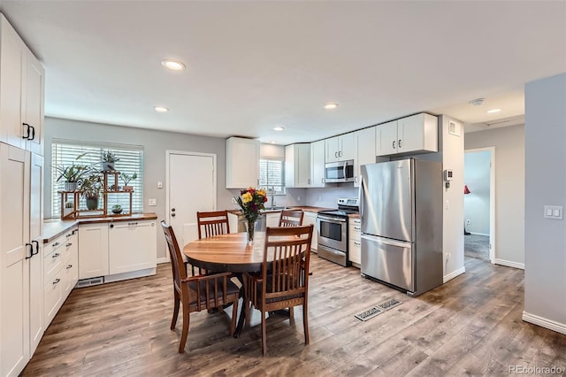 kitchen featuring a healthy amount of sunlight, white cabinetry, stainless steel appliances, and wood finished floors