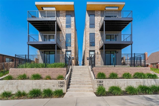 view of front of home featuring fence, a balcony, and stone siding
