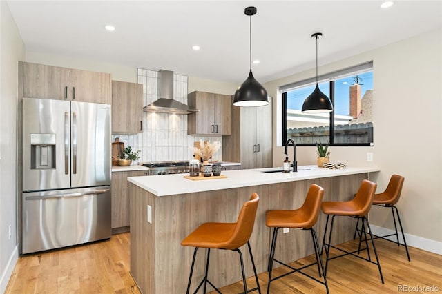 kitchen with a peninsula, a kitchen breakfast bar, stainless steel fridge, wall chimney exhaust hood, and a sink
