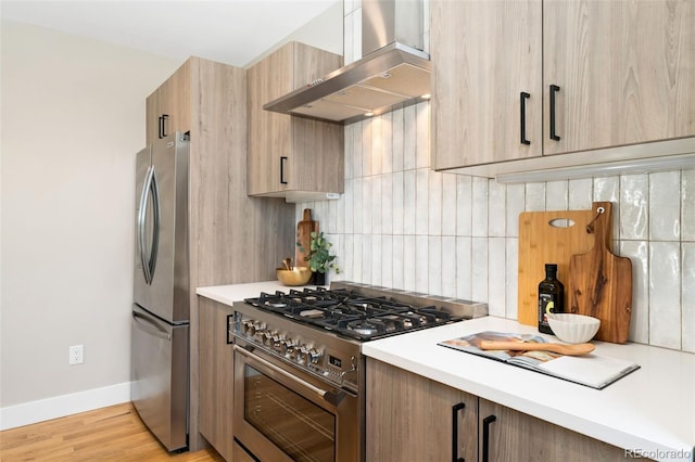 kitchen featuring backsplash, appliances with stainless steel finishes, light countertops, baseboards, and wall chimney exhaust hood
