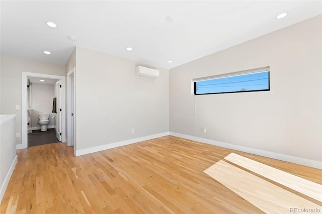 spare room featuring recessed lighting, baseboards, light wood finished floors, and an AC wall unit