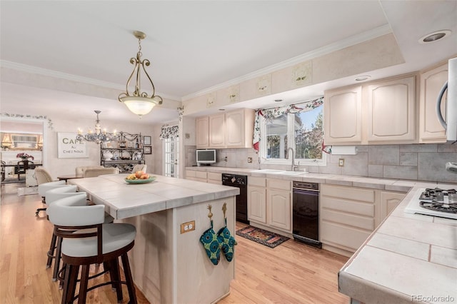 kitchen with tile countertops, sink, hanging light fixtures, light wood-type flooring, and a kitchen island