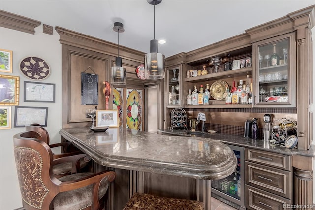 bar featuring hanging light fixtures, dark brown cabinetry, beverage cooler, and dark stone counters