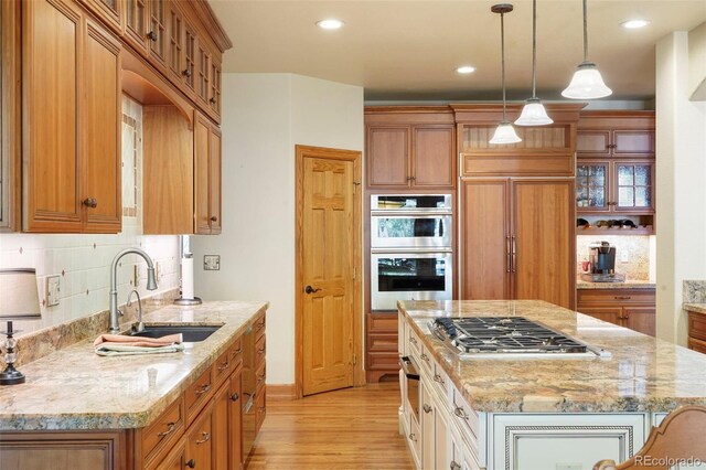20050 Lost Arrowhead Dr, Monument, CO 80132 - kitchen with appliances with stainless steel finishes, a sink, light wood-style floors, tasteful backsplash, and light stone countertops