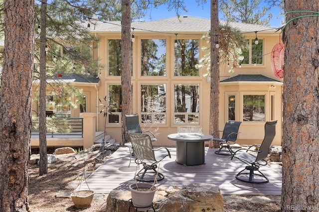 20050 Lost Arrowhead Dr, Monument, CO 80132 - back of property featuring a shingled roof, an outdoor fire pit, a wooden deck, and stucco siding