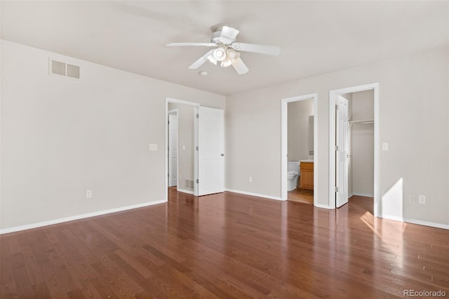 unfurnished bedroom with a walk in closet, ceiling fan, ensuite bathroom, dark wood-type flooring, and a closet