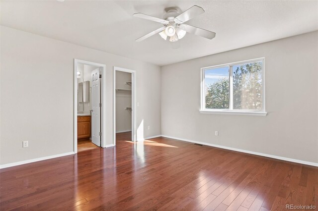 unfurnished bedroom featuring ceiling fan, wood-type flooring, connected bathroom, a closet, and a walk in closet