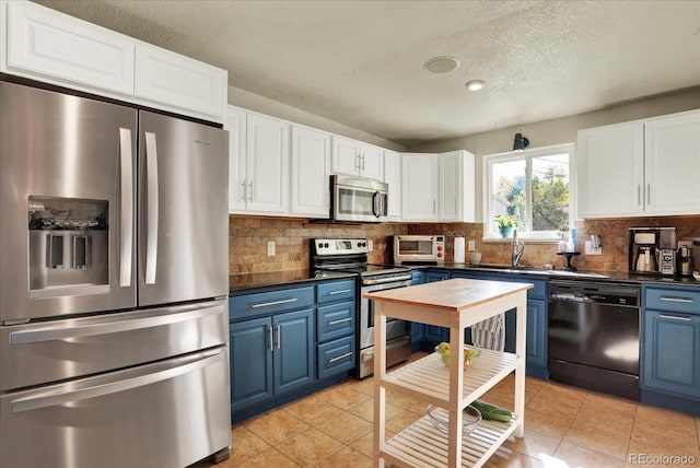 kitchen featuring sink, light tile patterned floors, blue cabinetry, appliances with stainless steel finishes, and white cabinetry