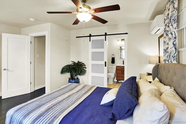 bedroom with ensuite bath, ceiling fan, a wall mounted air conditioner, a barn door, and dark hardwood / wood-style floors