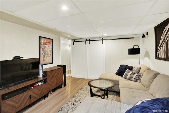 living room with a drop ceiling, a barn door, and light wood-type flooring