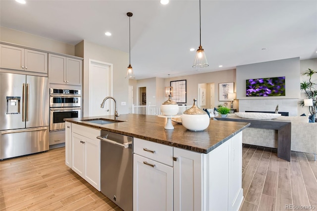 kitchen with a kitchen island with sink, a sink, open floor plan, appliances with stainless steel finishes, and light wood finished floors