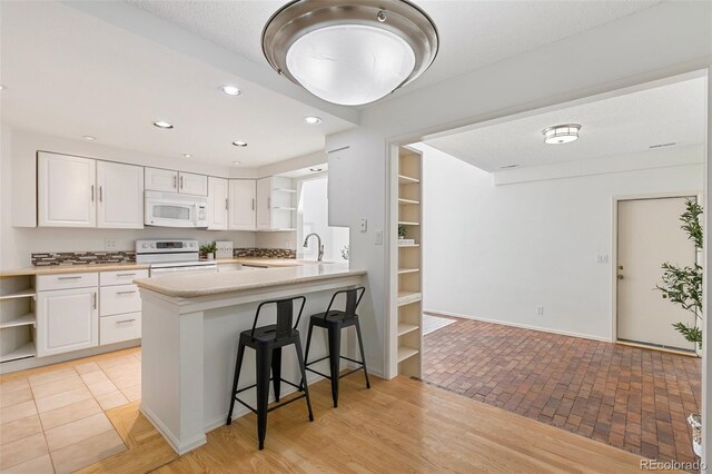 2049 Sussex Ln, Colorado Springs, CO 80909 - kitchen with white appliances, open shelves, white cabinetry, a kitchen breakfast bar, and light countertops