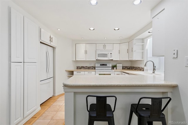 2049 Sussex Ln, Colorado Springs, CO 80909 - kitchen with white appliances, open shelves, a peninsula, white cabinetry, and a kitchen breakfast bar