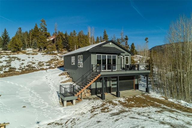 snow covered rear of property with stairs and a wooden deck