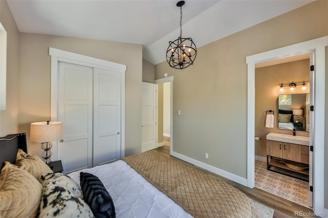 bedroom with ensuite bathroom, wood finished floors, baseboards, vaulted ceiling, and a closet