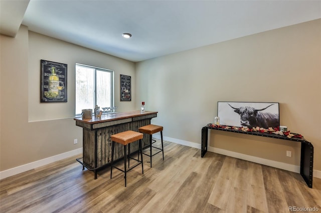 bar featuring a bar, light wood-style floors, and baseboards