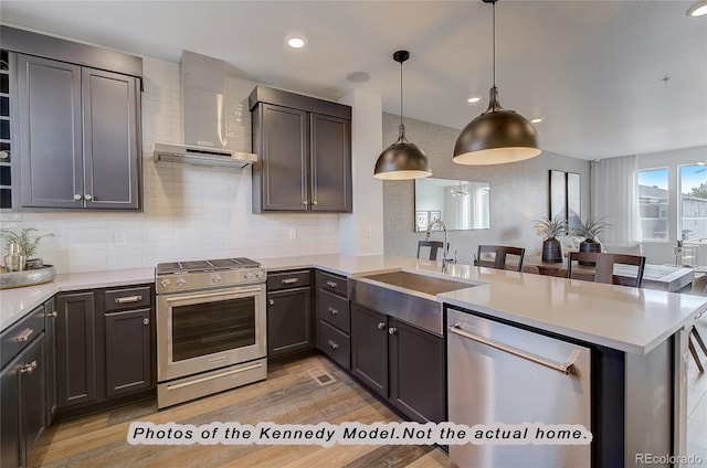 kitchen featuring sink, hanging light fixtures, kitchen peninsula, stainless steel appliances, and wall chimney range hood