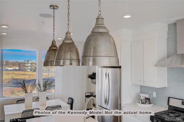 interior details with stainless steel appliances, tasteful backsplash, wall chimney exhaust hood, and decorative light fixtures