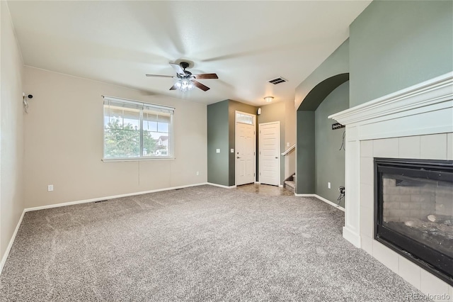 unfurnished living room featuring a tiled fireplace, carpet flooring, and ceiling fan