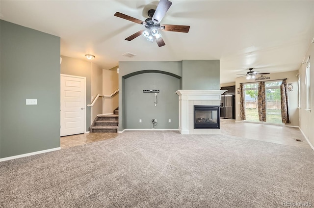 unfurnished living room with a tiled fireplace, light carpet, and ceiling fan