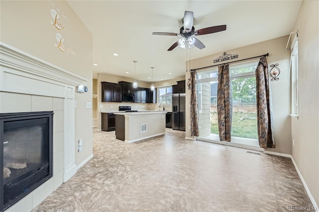 unfurnished living room with a tiled fireplace, sink, a wealth of natural light, and ceiling fan