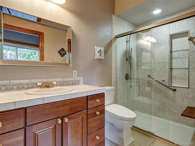 6533 S Quemoy Way, Aurora, CO 80016 - bathroom featuring toilet, vanity, tile patterned flooring, a textured wall, and a shower stall