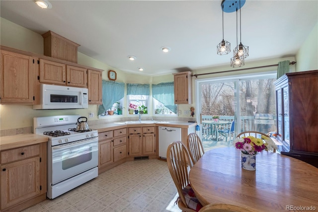 kitchen featuring light countertops, hanging light fixtures, light brown cabinetry, a sink, and white appliances