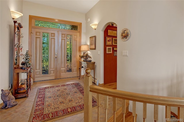 entryway featuring baseboard heating, arched walkways, light tile patterned floors, and stairs