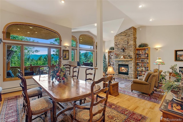 dining space with a stone fireplace, high vaulted ceiling, wood finished floors, and baseboard heating
