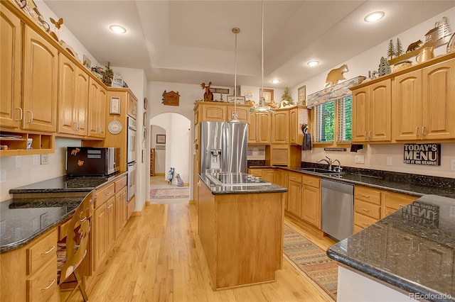 kitchen featuring a center island, arched walkways, a sink, light wood-style floors, and stainless steel appliances
