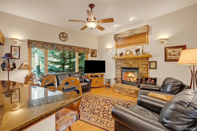 living area with a stone fireplace, light wood-style flooring, and ceiling fan