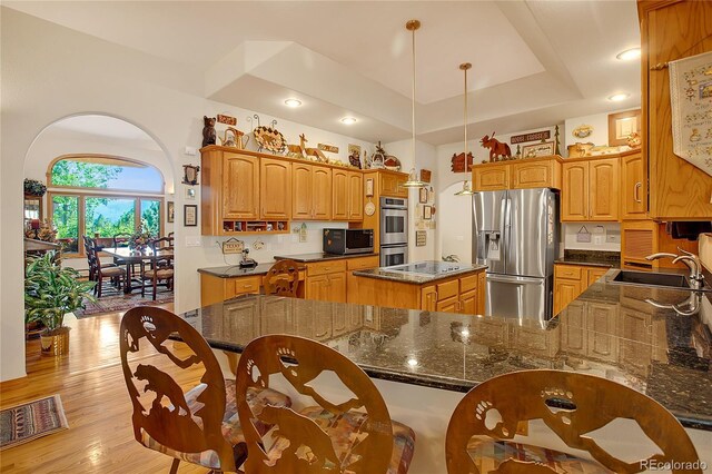 kitchen with a sink, a tray ceiling, stainless steel appliances, light wood-style flooring, and decorative backsplash