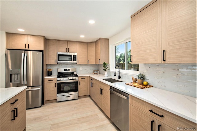 kitchen with sink, decorative backsplash, light stone countertops, light brown cabinetry, and appliances with stainless steel finishes