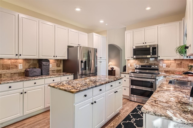 kitchen featuring light hardwood / wood-style flooring, light stone countertops, a center island, white cabinetry, and appliances with stainless steel finishes